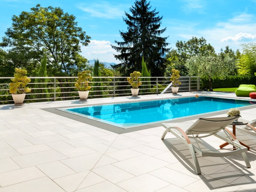 Outdoor swimming pool with sandstone floors and veranda with beautiful green trees and grass view