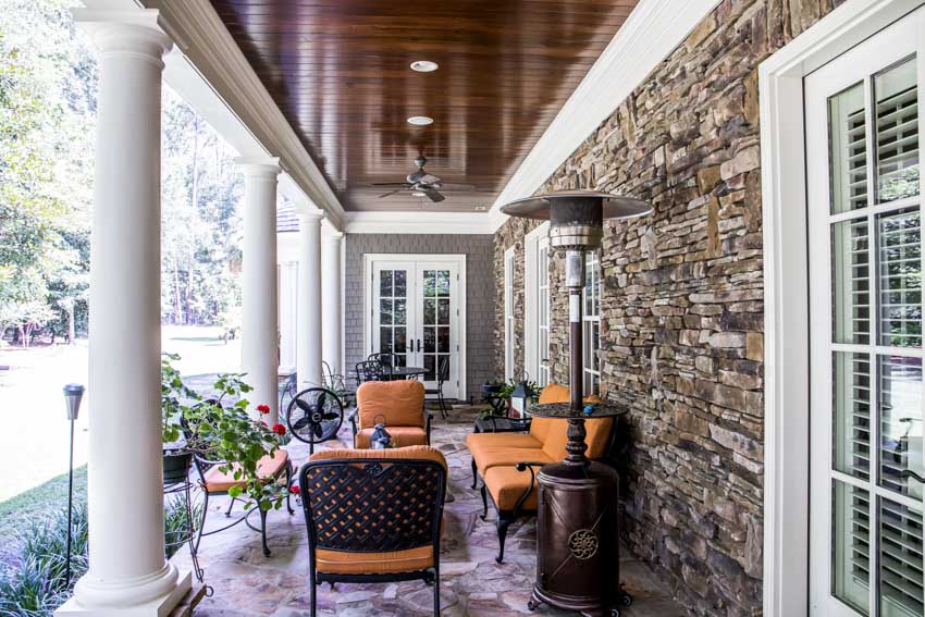 Patio with outdoor ceiling panels, cushioned chairs, heater, stone wall cladding, and windows