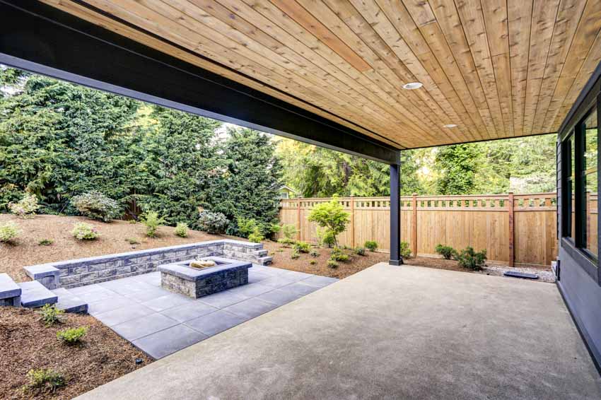 Patio with outdoor wood ceiling panels, concrete deck, wooden fence, and firepit