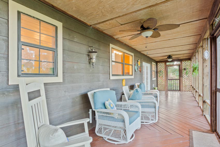 Porch area with plywood overhead, chairs, siding, windows, and ceiling fan