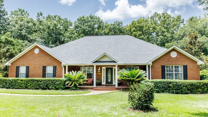Red brick house with window shutters, spacious lawn and trees with lots of curb appeal
