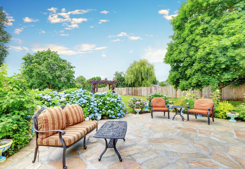 A relaxing patio area with faux stone flooring, comfortable outdoor furniture and blooming hydrangea flowers