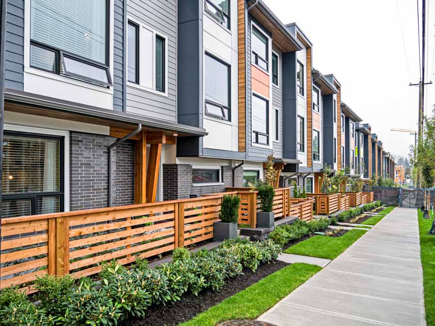 Row of apartment properties with pressure treated split rail fence, hedge plants, and walkway