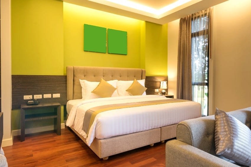 Simple bedroom interior with lime green walls, panoramic windows, bed, and wood flooring
