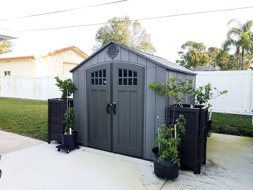 Small black shed with doors, potted plants, and fence