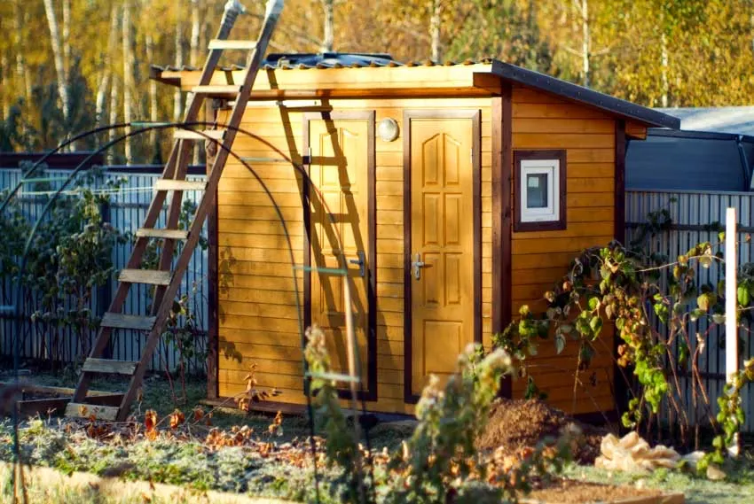 Small wooden shed with door and angled roof near a metal fence