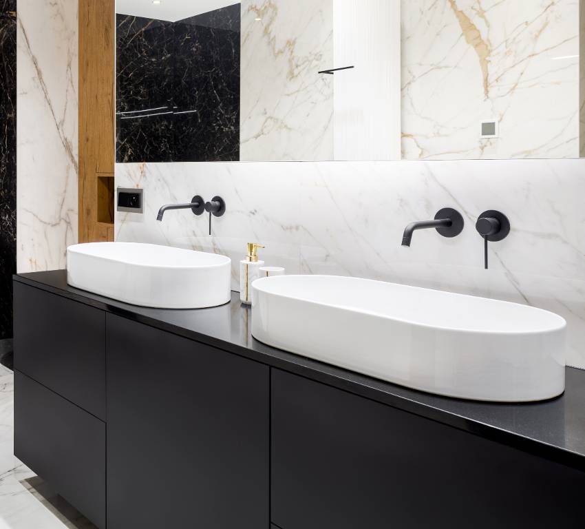 Stunning bathroom with white marble tiles, mirror washbasins and black granite countertop 