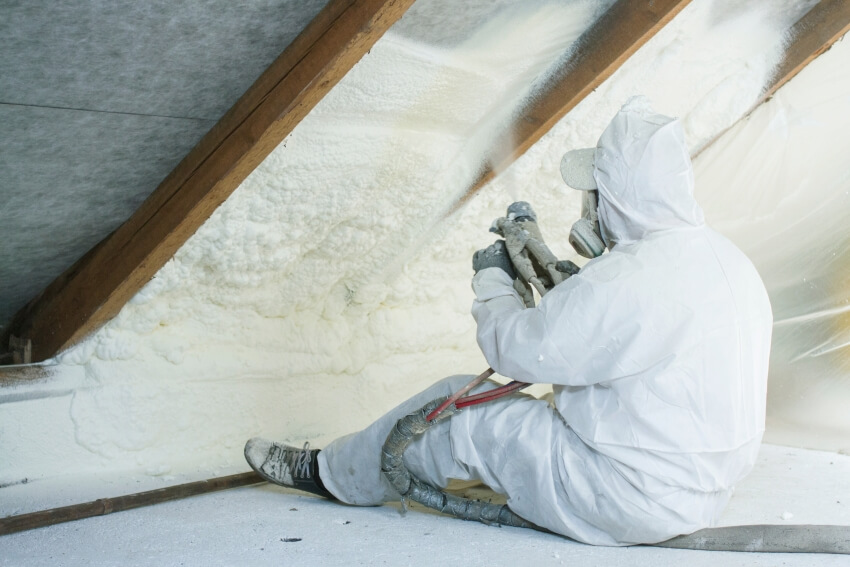 Technician spraying foam insulation on roof using plural component gun