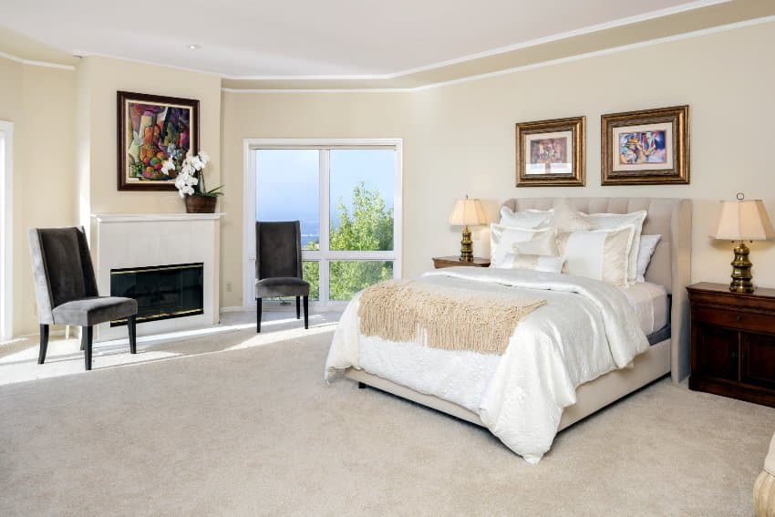 Traditional cream color bedroom interior with huge glass windows, gray chairs, and a bed with side tables and lamps
