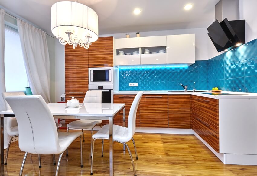 White and wooden kitchen with dining set, teak veneer cabinets, white countertops and blue tile backsplash