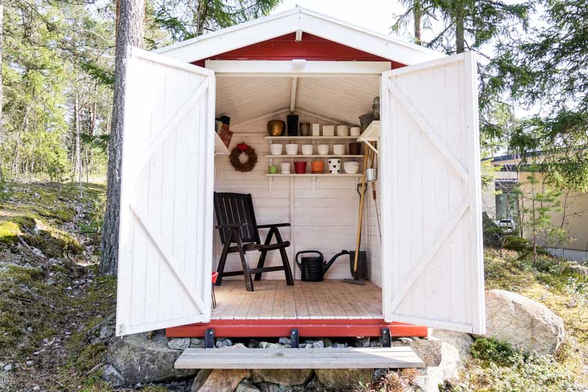White outdoor shed with chair, shelves, and tools inside it