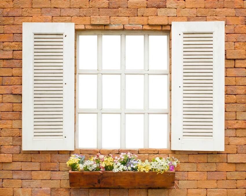 White window with white shutters on brick wall with flowers in the box for design 