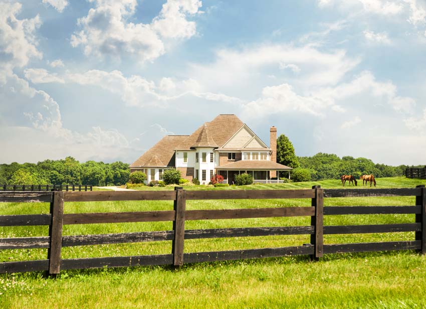 Wooden split rail fence surrounding a farmhouse with pitched roof and trees