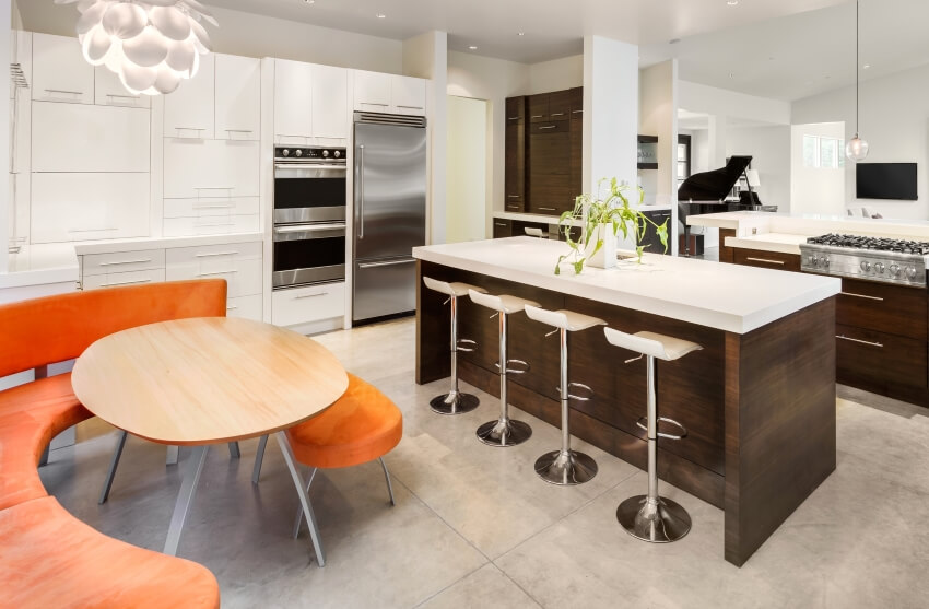 A bright kitchen with large island, tile floors, and an orange sitting area with table