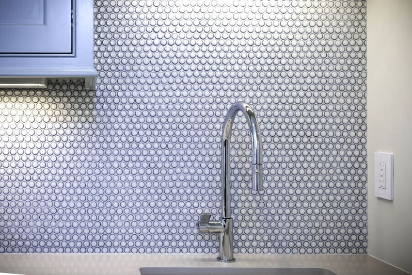 A sink, a silver faucet, and a gray penny tile backsplash in a kitchen interior