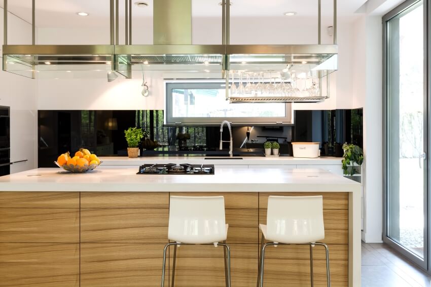 Aluminum cabinet and exhaust hood and glass rack over island with a cooktop in a bright kitchen
