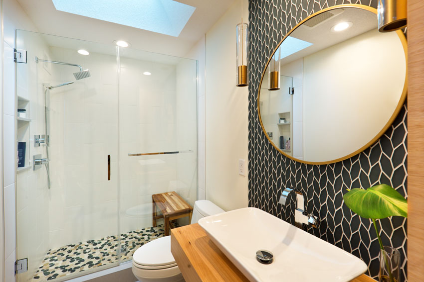 Bathroom with braided picket tile backsplash, mirror, sink, shower area, glass door, shower bench, and toilet