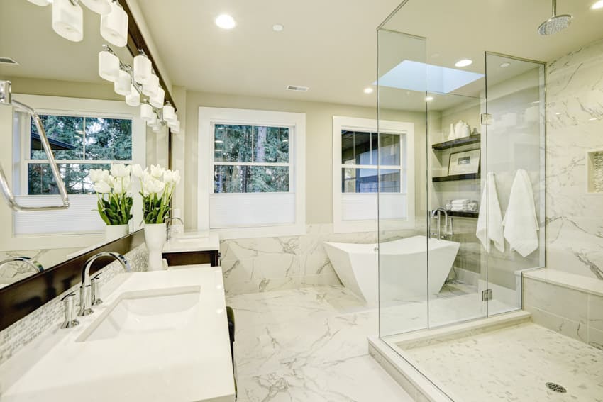 Bathroom with Carrara marble walls, floors, glass shower enclosure, sink, countertop, windows, and mirror