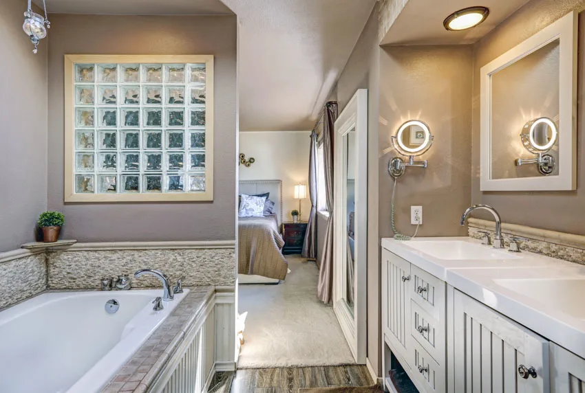 Bathroom with taupe walls, tub, frosted glass, countertop, mirror, sink, faucet, and lighting fixtures