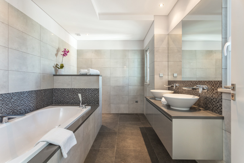 Bathroom with tub, vanity mirror, countertop, sink, matte porcelain tile flooring, and wall