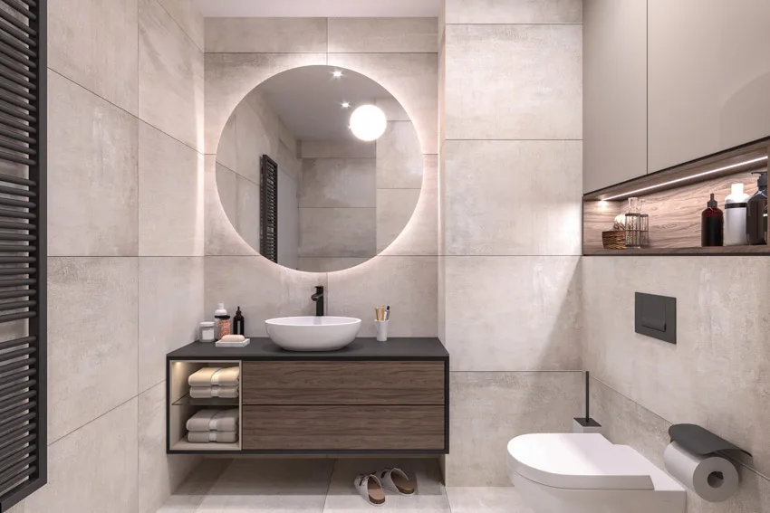 Bathroom with large wall tiles, round mirror with illumination and wooden vanity shelf