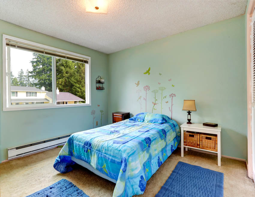 Bedroom with aqua green wall, comforter, pillows, window, heater, nightstand, and lamp