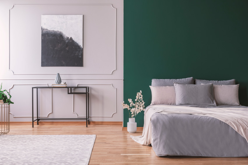 Green and white wall with wainscoting and blush colored pillows on grey bed