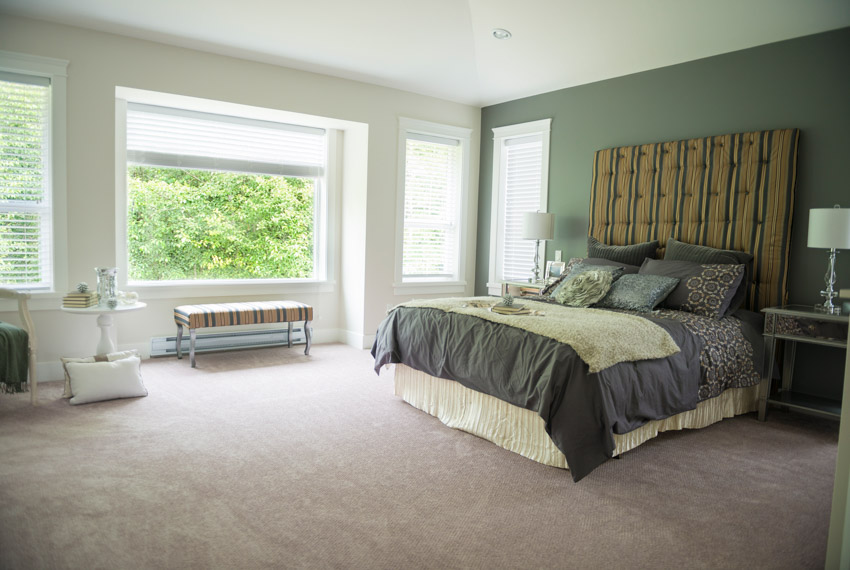 Bedroom with dark green wall, headboard, pillows, comforter, nightstand, lamp, and windows