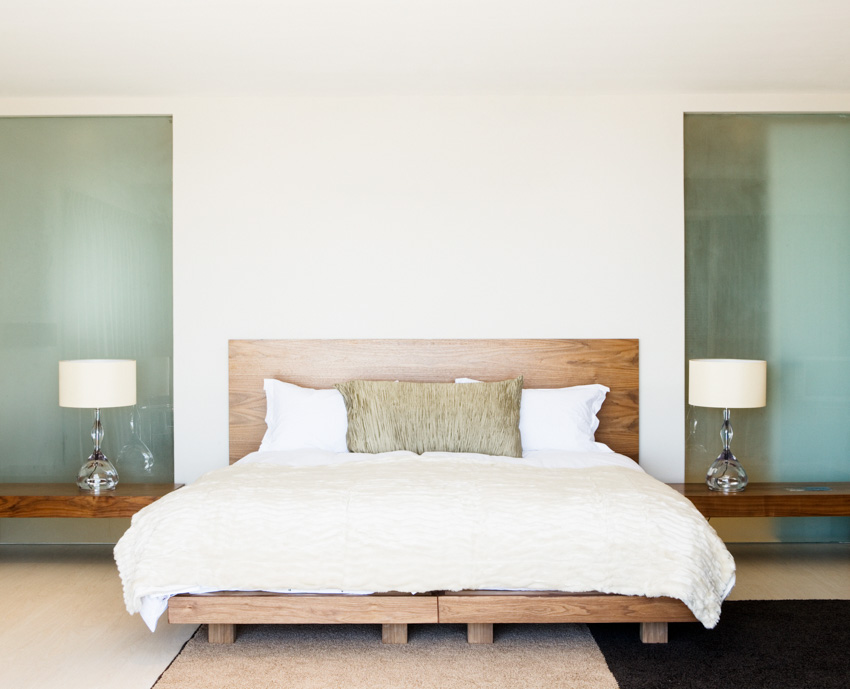 Bedroom with floating nightstands, lamp, wood headboard, and coverlet bedding