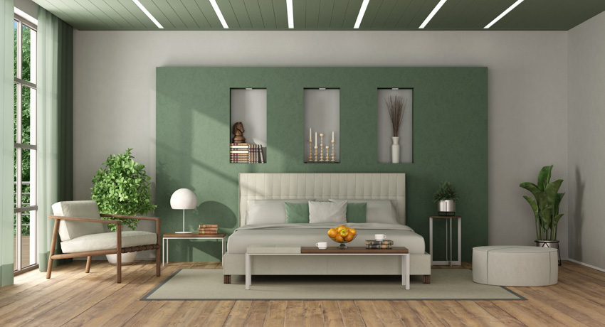 Bedroom with hunter green accent wall, bed, pillows, headboard, wood floor, chair, nightstand, lamps, indoor plants, and window