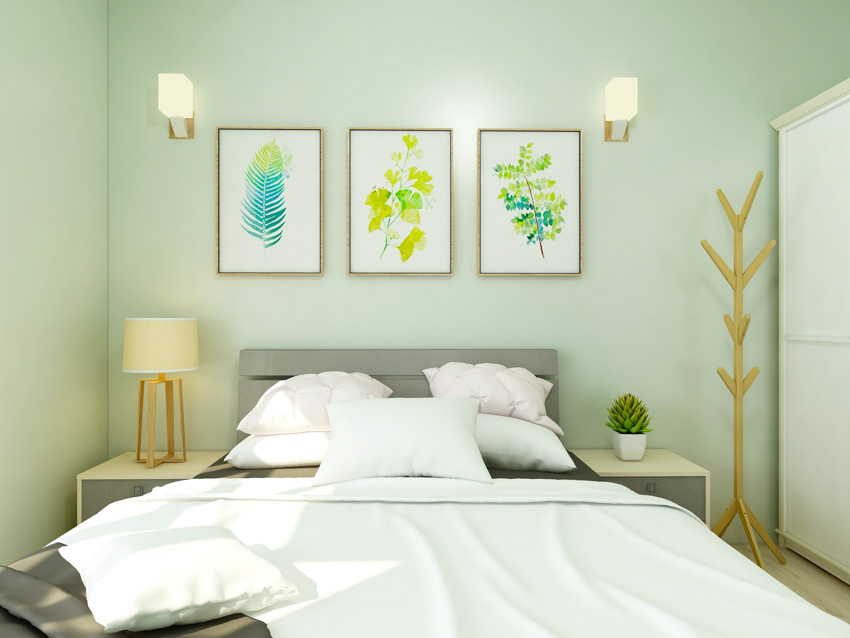 Bedroom with light green wall, bed, pillows, nightstand, lamp, and lighting fixtures