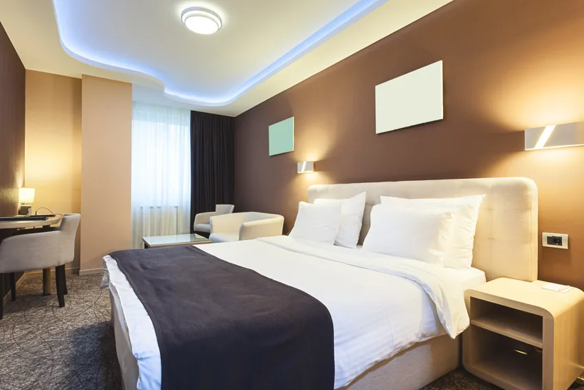 Bedroom with nightstand, lamps, bedding, headboard, pillows, curtains, and taupe walls