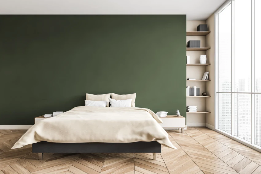 Bedroom with olive hued wall, white pillows, shelves and herringbone pattern floors