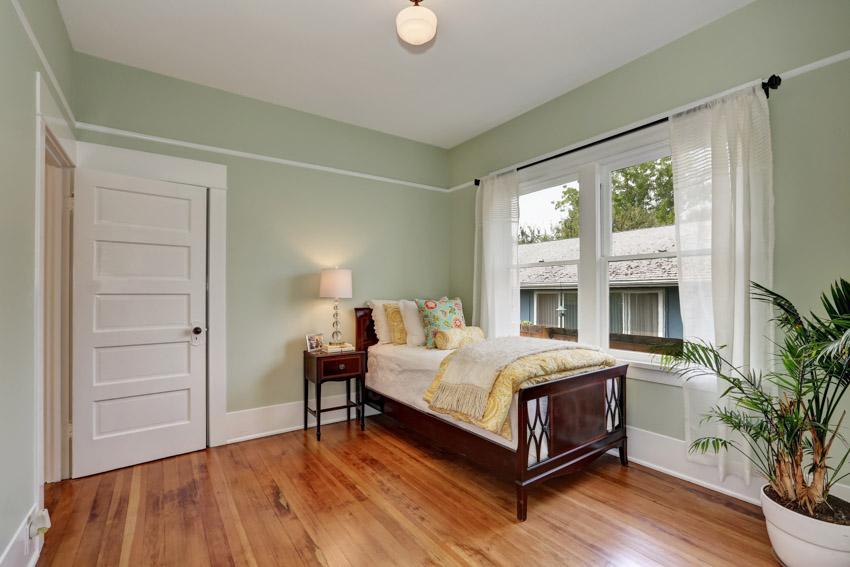 Mahogany bedframe, palm plant, white door and large window with curtains