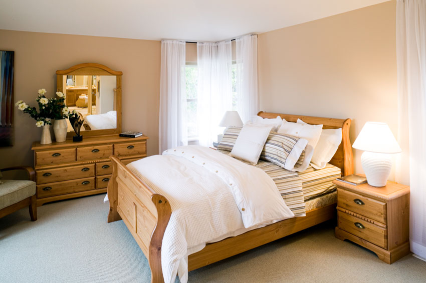Bedroom with wood nightstand, footboard, headboard, comforter, bedding, pillows, vanity, mirror, and drawers