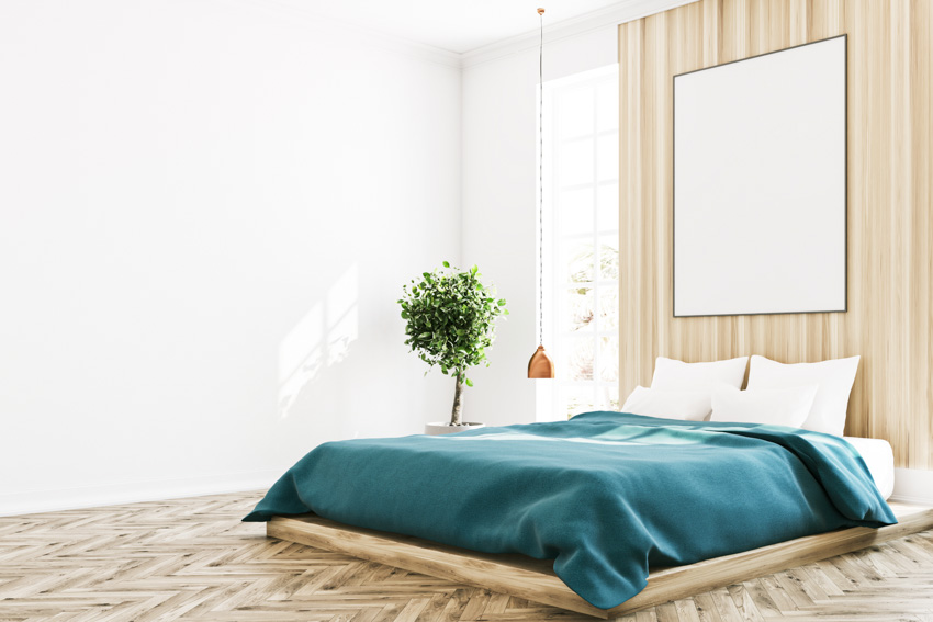 Bedroom with wooden floor, polyester bedding, pillows, wood accent wall, and indoor plant