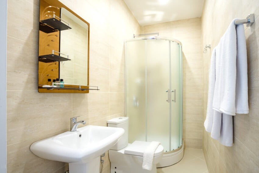 Beige bathroom with translucent frosted shower glass door, mirror over the sink towel and toilet