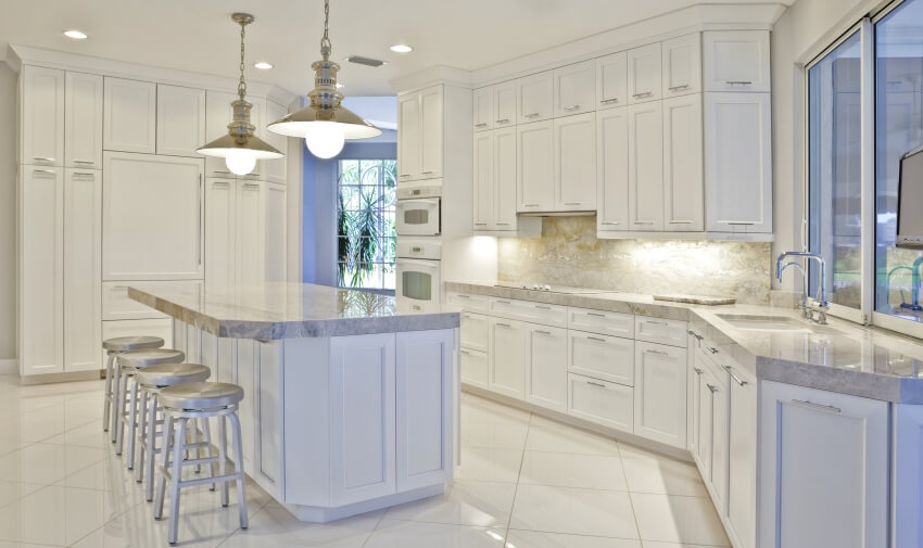 Bright empty kitchen with pendant lights over island, marble countertops, and ceiling height cabinets