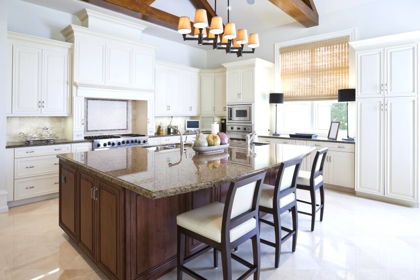 Bright kitchen with white cabinets and chandelier over large island with dark brown granite countertops
