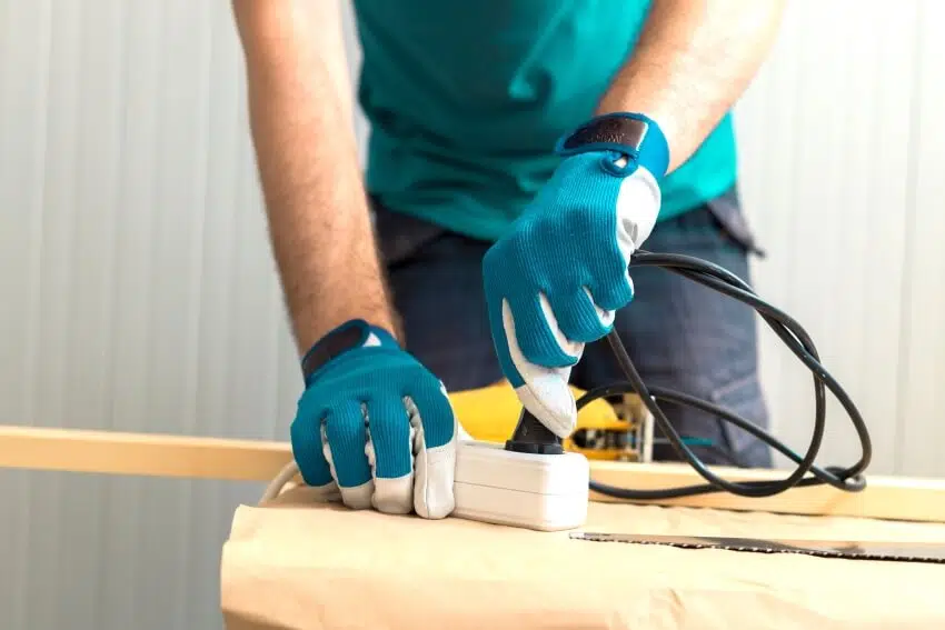 Carpenter handyman with hand gloves plugging electric handy saw into an extension cord