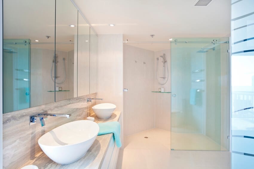 Cream bathroom iwith two wash basins and shower with sliding doors made of glass