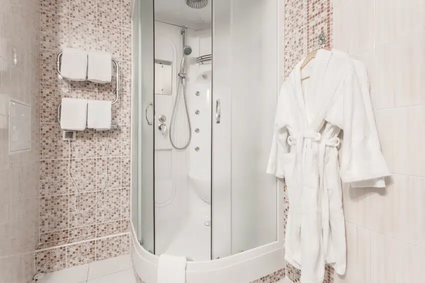 A clean white towel and bathrobe on a hanger beside an enclosed shower with frosted glass doors