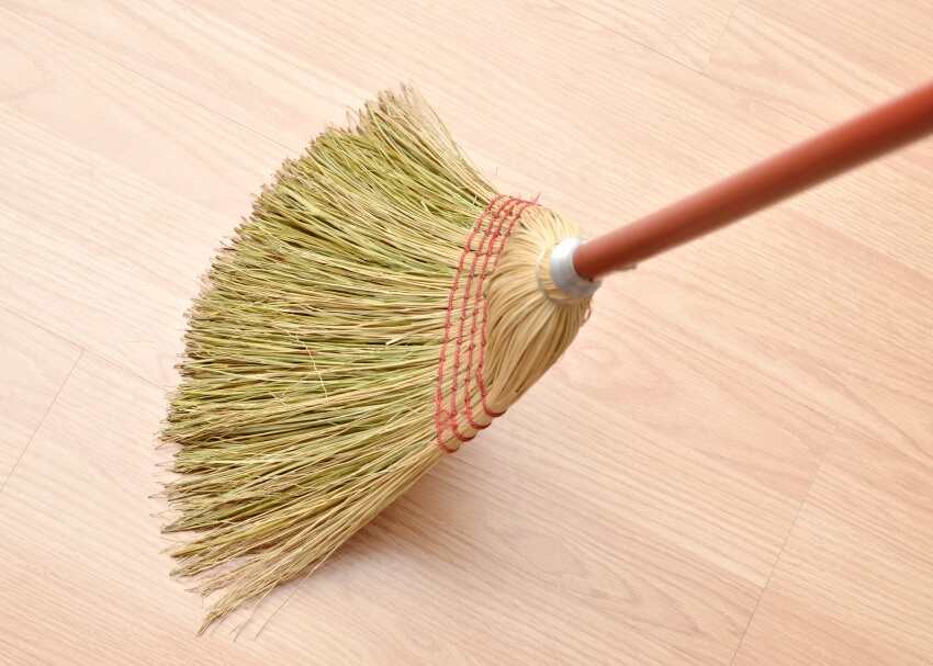 A close up of a straw broom sweeping a laminate floor 