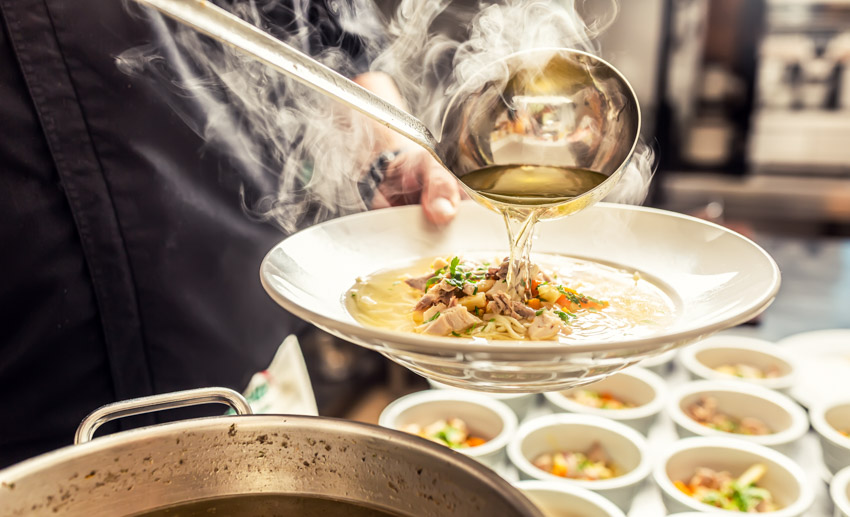 Cook pouring hot soup onto a soup plate