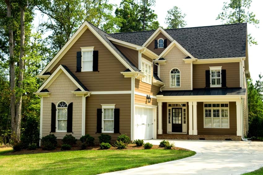Dark brown house exterior with dormer, driveway, windows, hedge plants, and front door