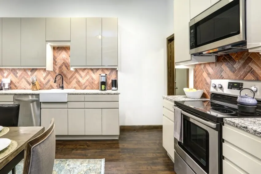 Open layout kitchen space with shiny beige cabinets and herringbone backsplash