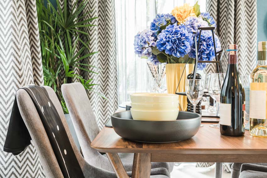 Room with chairs, curtains, table with bowls, centerpiece, and wine bottles