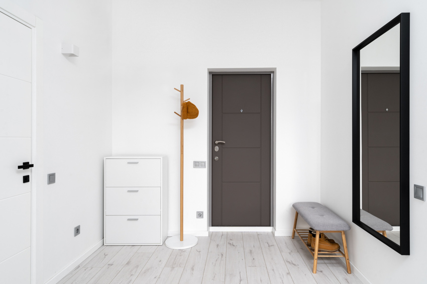 Empty room with black interior door, white trim, mirror, small chair, stand drawer, and white walls