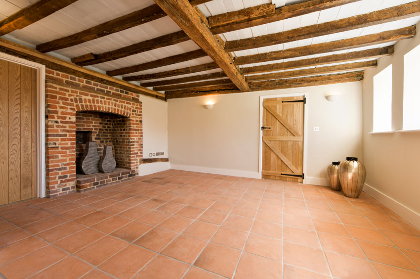 Empty room with exposed wood ceiling, fireplace, wooden door, windows, and Saltillo tile floors