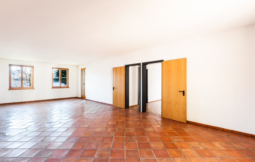 Empty room with glazed terracotta tile floor, doors, white walls, and windows